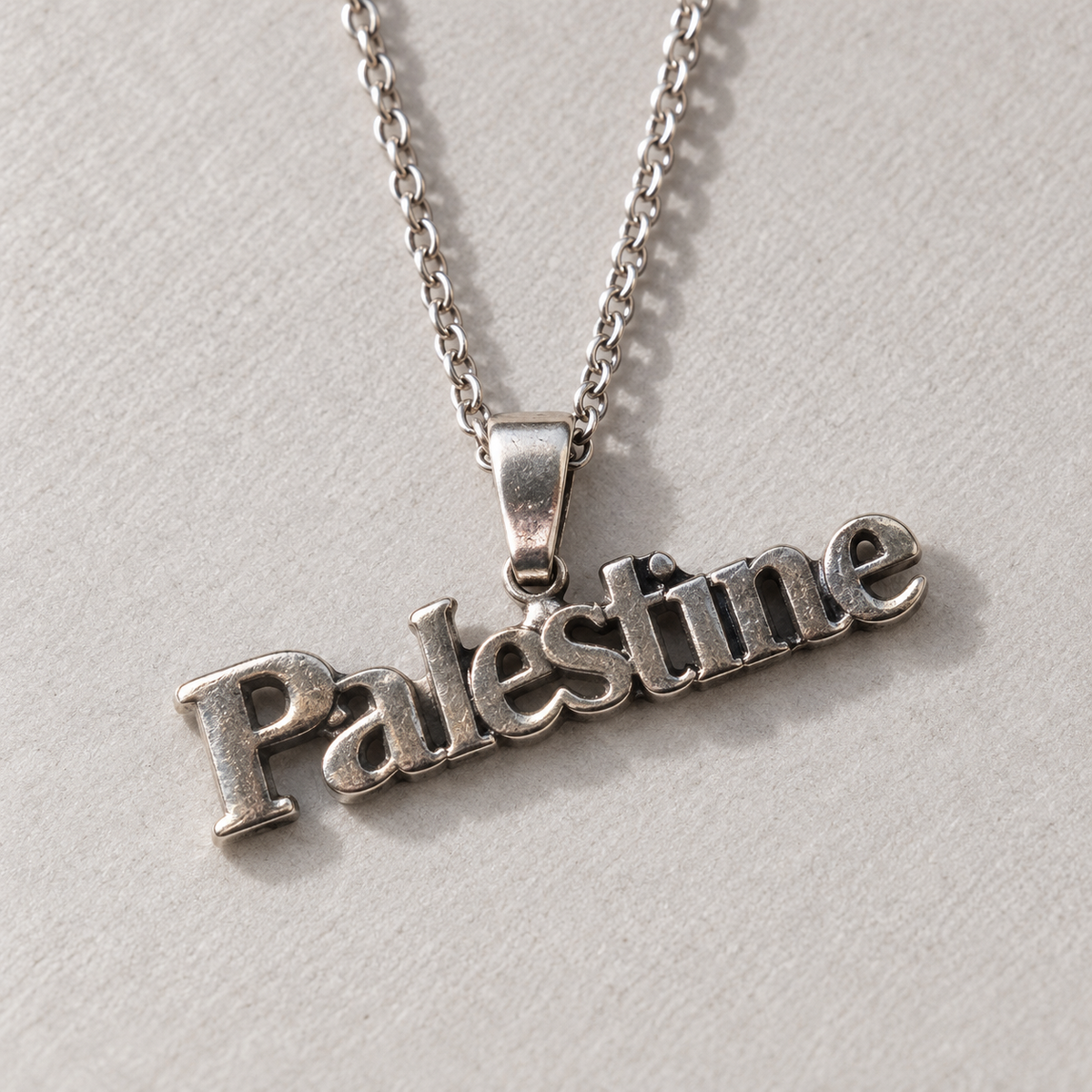 Close-up of the joined Palestine lettering and central bail on a silver-tone necklace.